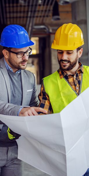Empresas Dos trabajadores de construcción revisan un plano, usando cascos y chalecos de seguridad.