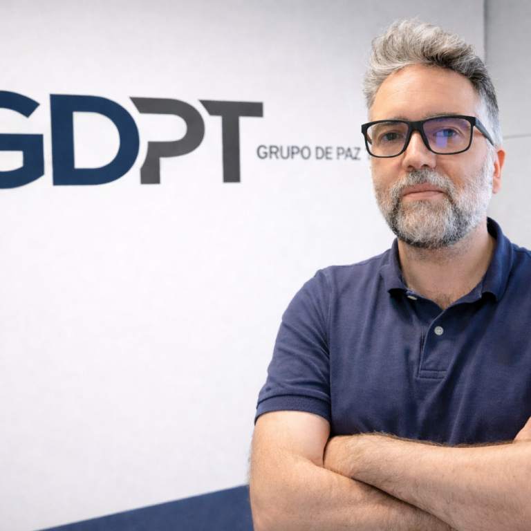 Eduardo de Paz Hombre con gafas y cabello gris, de brazos cruzados, de pie junto a un logo.
